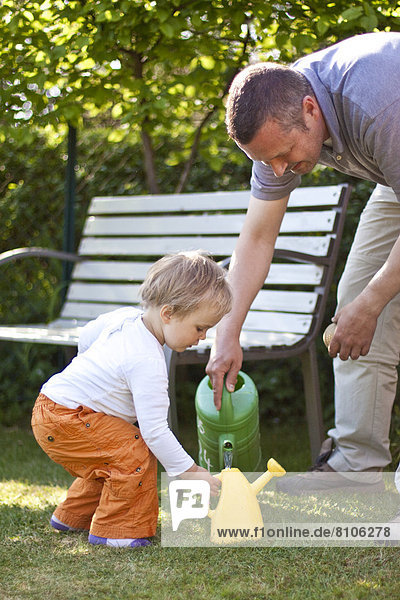 Kleinkind und Vater im Garten gießen Blumen