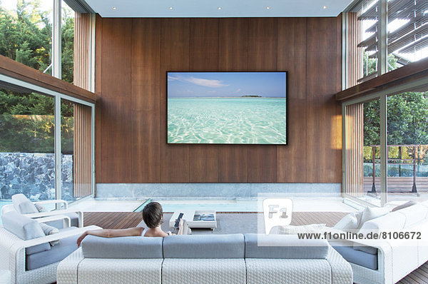 Frau schaut einen großen Flachbildschirm im modernen Wohnzimmer an