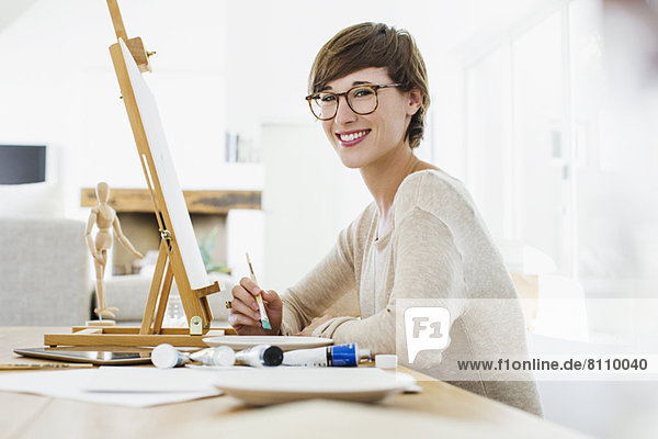 Portrait of smiling woman painting at easel on table