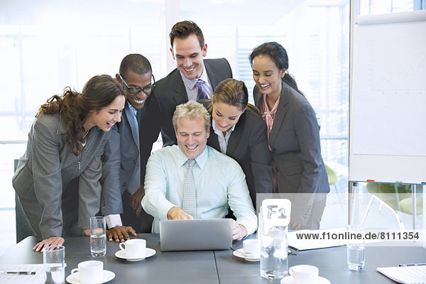 Smiling business people sharing laptop in conference room
