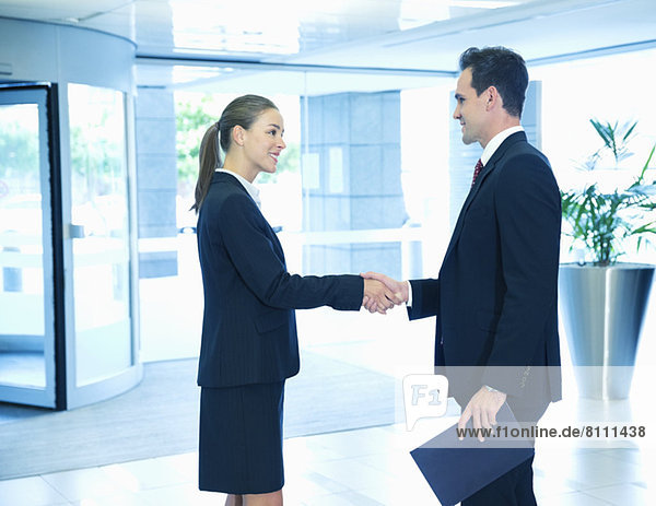 Smiling businessman and businesswoman handshaking in lobby