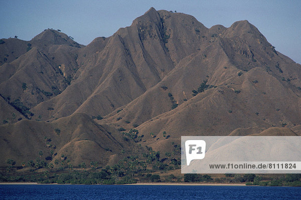 Asia Indonesia Sky Mountains Cliffs Terrain Grass Plants Water Sea Nobody Still Uneven Rugged Hard Slope Rough Steep Outdoors Day Front View Horizontal Color Image Photography