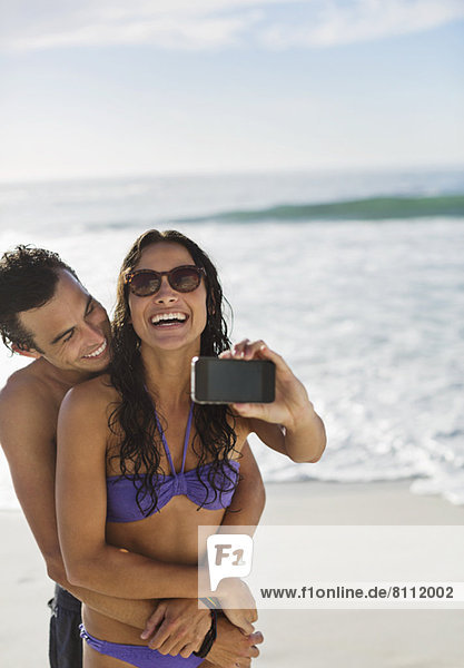 Glückliches Paar beim Selbstporträt mit Fotohandy am Strand