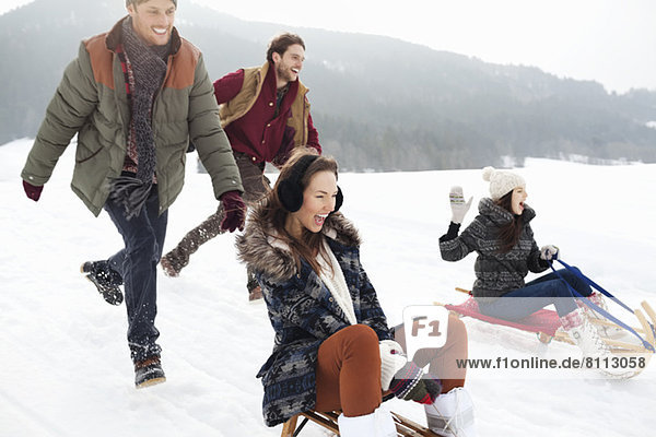 Enthusiastic friends sledding in snowy field