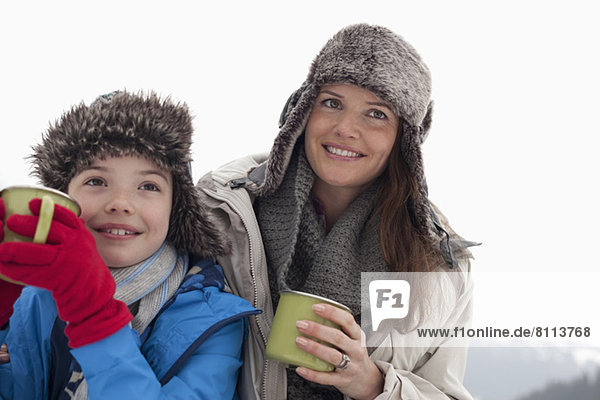 Happy mother and son in fur hats drinking hot chocolate