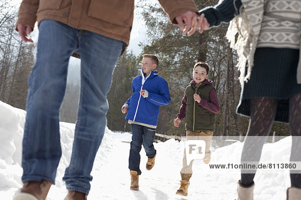 Boys running behind parents holding hands in snow