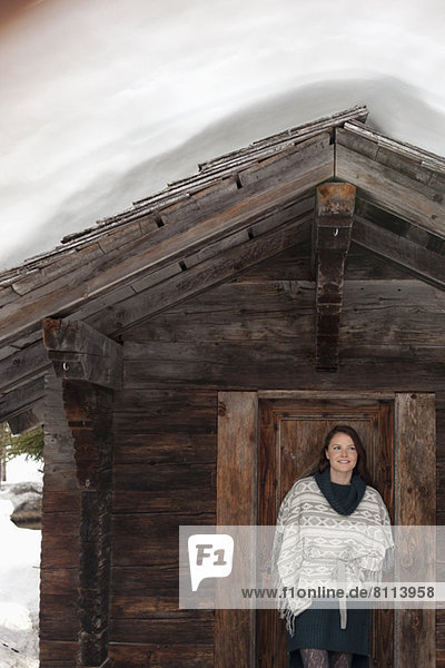 Portrait of smiling woman standing in doorway of snowy cabin