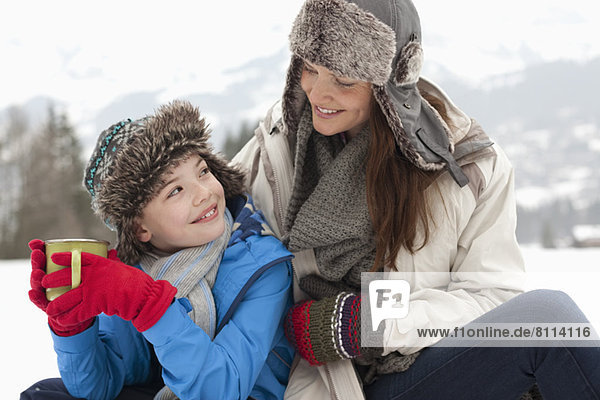 Happy mother and son drinking hot chocolate in snowy field