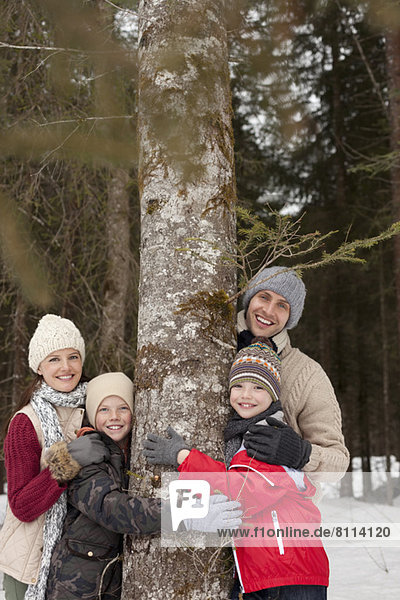 Portrait of happy family hugging tree trunk in snowy woods