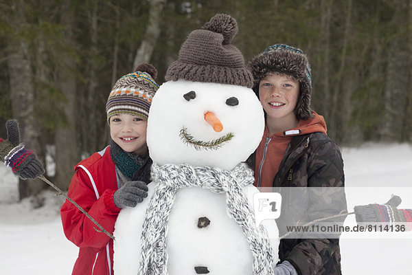 Portrait of happy boys posing with snowman