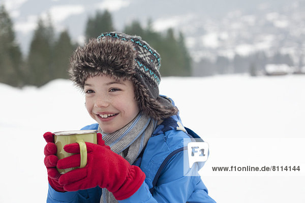 Happy boy drinking hot chocolate in snowy field