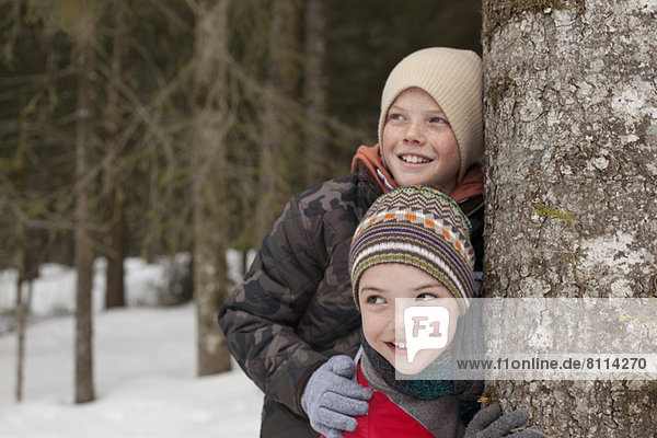 Happy boys leaning against tree trunk in snowy woods
