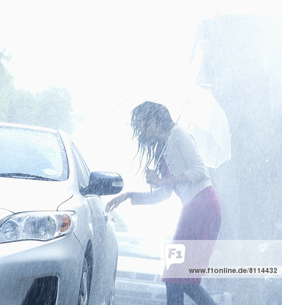 Woman with umbrella reaching for car door handle in rain
