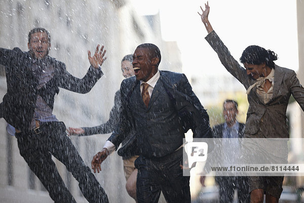 Enthusiastic business people running in rainy street