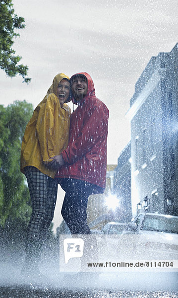 Happy couple in raincoats holding hands in rain