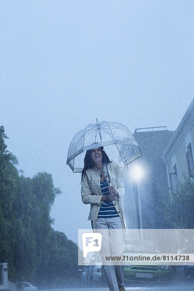 Fröhliche Frau mit Regenschirm  die im Regen läuft