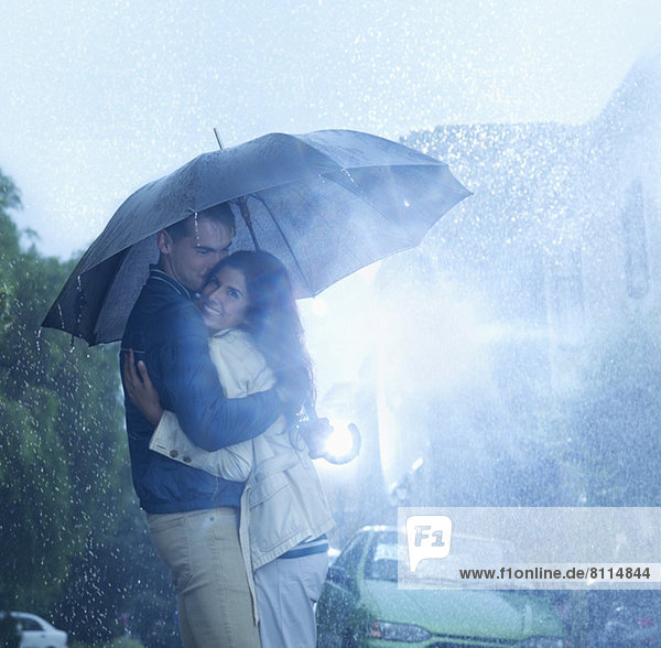 Glückliches Paar  das sich unter dem Regenschirm umarmt.