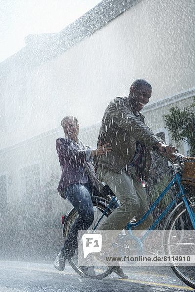 Happy couple riding bicycle in rainy street