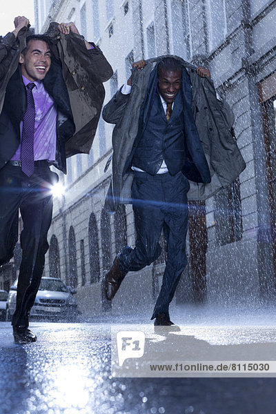 Happy businessmen covering heads with coats in rainy street