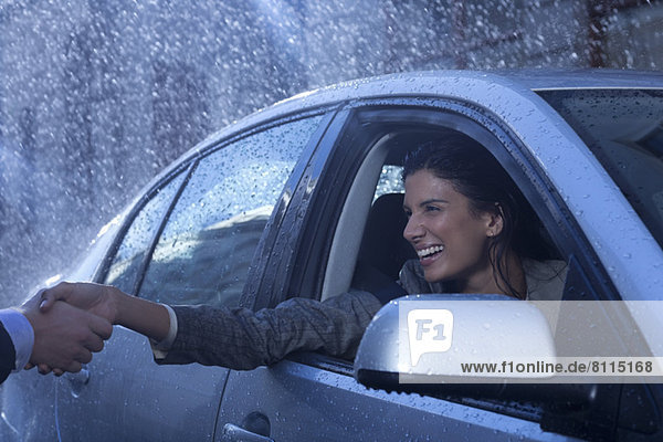 Smiling businesswoman in car extending handshake in rain