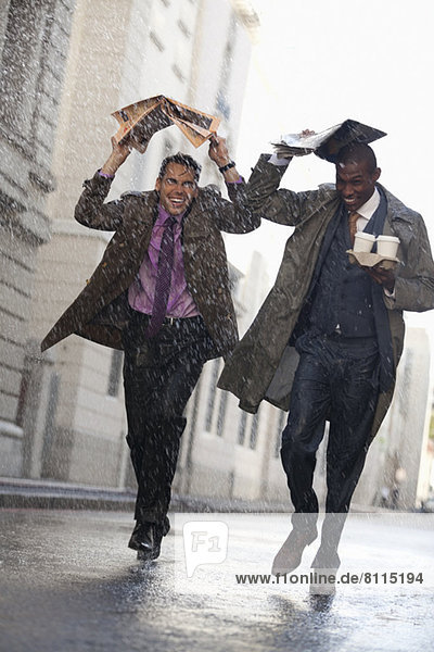 Businessmen with coffee covering heads with newspaper in rainy street