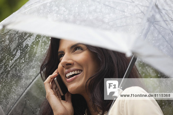 Happy woman talking on cell phone under umbrella in rain