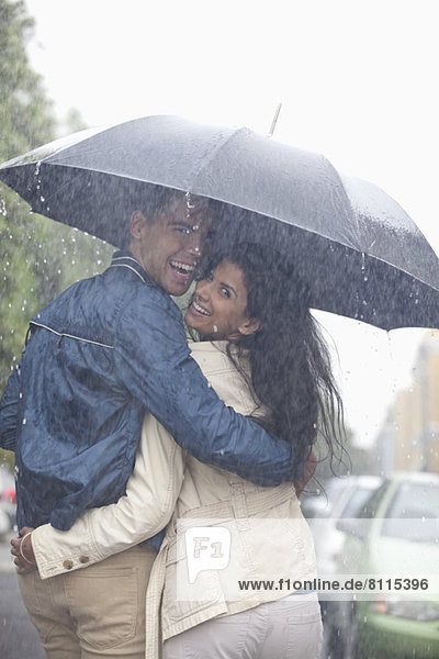 Portrait of happy couple hugging under umbrella in rain