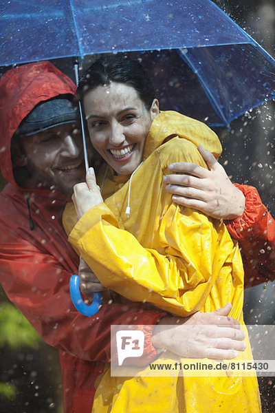 Happy couple hugging under umbrella in rain