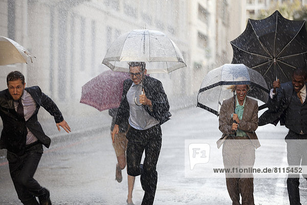 Enthusiastic business people with umbrellas running in rainy street