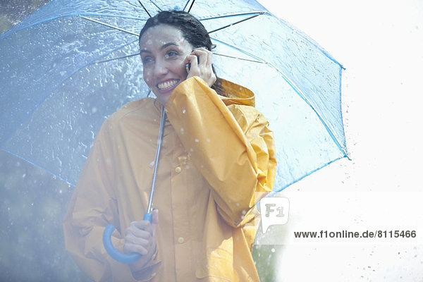 Happy woman talking on cell phone under umbrella in rain