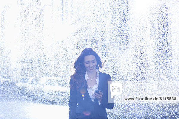 Happy businesswoman text messaging with cell phone in rain