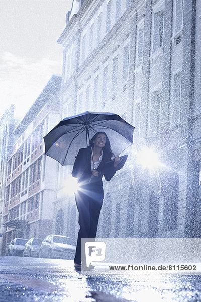 Businesswoman standing under umbrella in rainy street