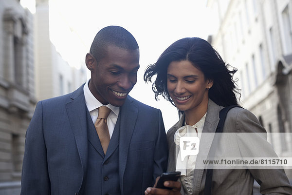 Smiling business people text messaging with cell phone