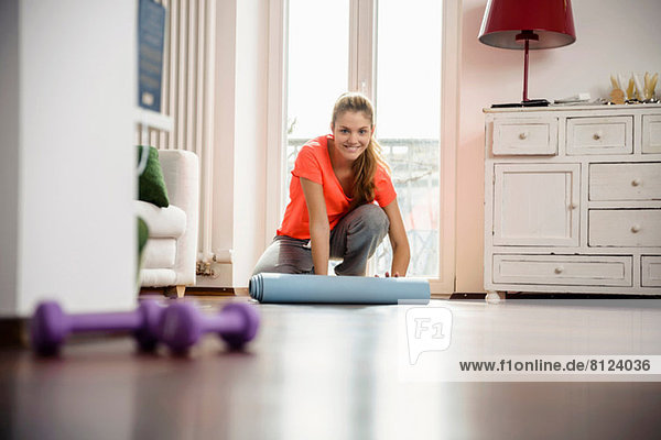 Young woman rolling up exercise mat at home