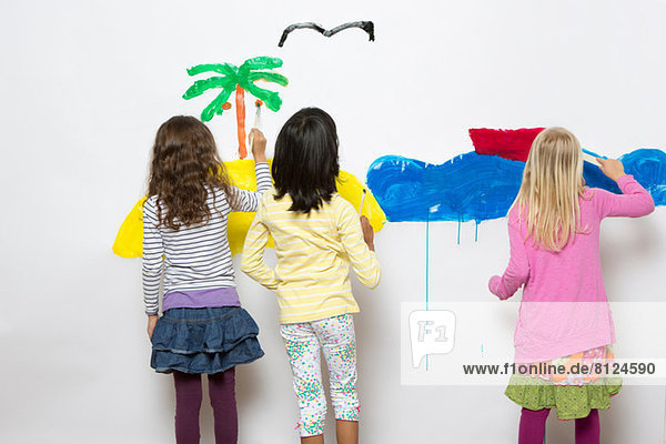 Drei Mädchen malen Ozean und Insel an der Wand