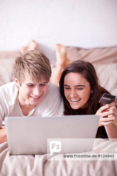 Junges Paar auf dem Bett liegend mit Blick auf den Laptop