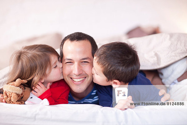 Sohn und Tochter küssen Väter Wange unter Bettdecke
