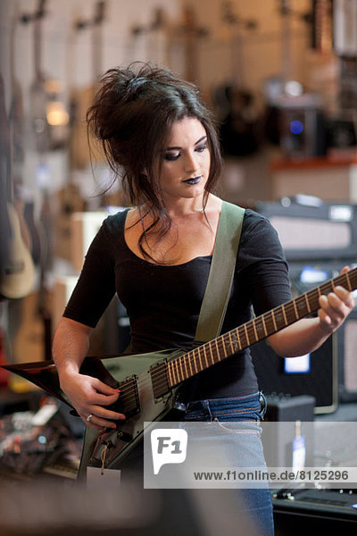 Young woman trying electric guitar in music store
