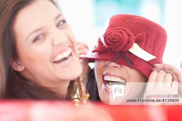 Zwei Freundinnen  die mit einem burgunderroten Hut herumspielen.