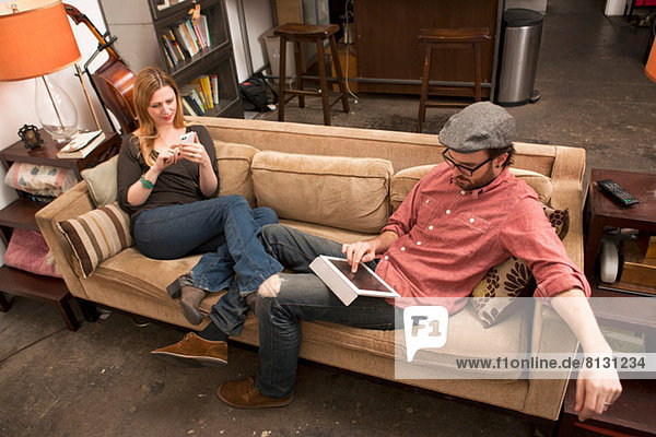 Couple sitting on sofa using digital tablet and smartphone