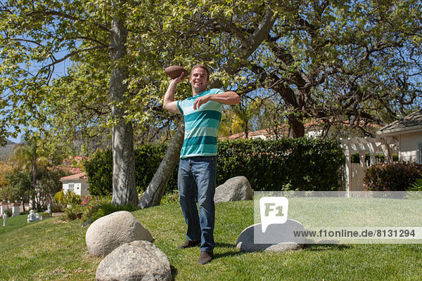 Junger Mann wirft American Football in den Garten