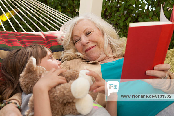 Grandmother and granddaughter reading book in hammock
