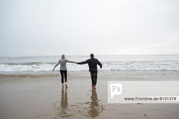 Ein reifes Paar hält sich am Strand an den Händen.