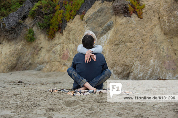 Erwachsenes Paar am Strand sitzend mit gekreuzten Beinen  Rückansicht