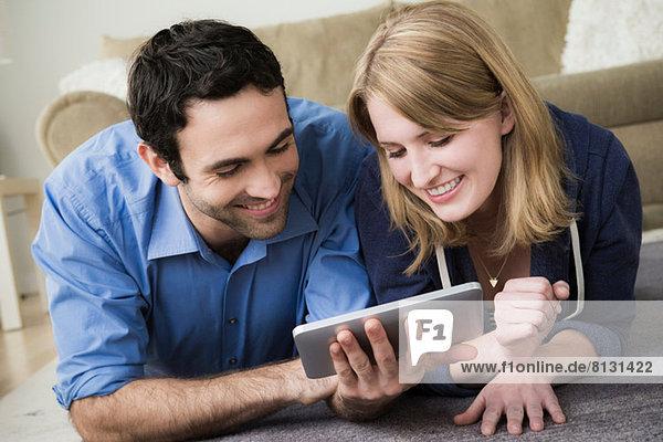 Junges Paar auf dem Boden liegend mit elektronischem Buch