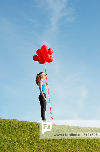 Teenagermädchen steht auf Gras und hält rote Luftballons.