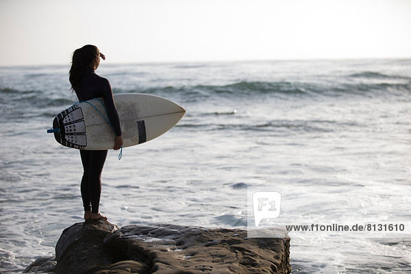 Junge Frau auf Felsen stehend mit Surfbrett