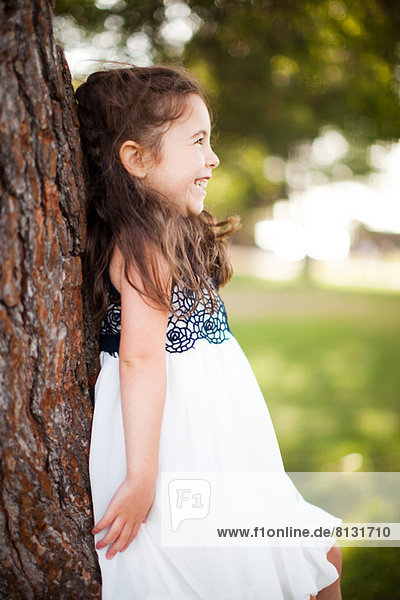 Portrait of girl leaning against tree trunk  smiling