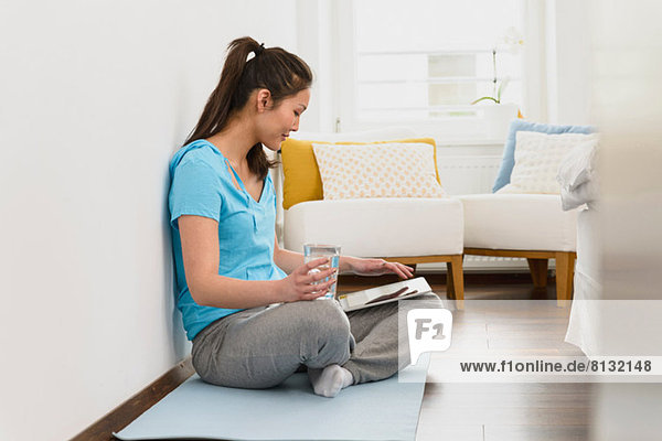 Frau auf Matte sitzend mit digitalem Tablett