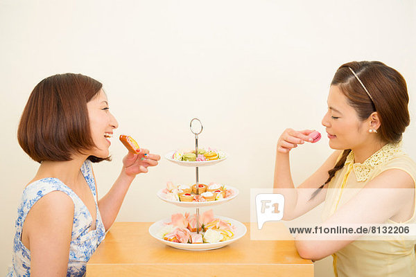 Two happy women enjoying dessert from three tiered cake stand